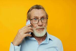 senior grijs haar Mens in een blauw overhemd en bril pratend Aan de telefoon geïsoleerd achtergrond foto