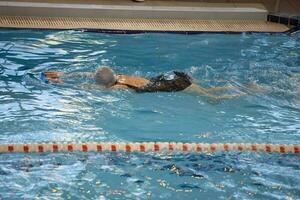 een vrouw zwemt in een zwart zwempak en een zwemmen pet zwemt in de zwembad. foto