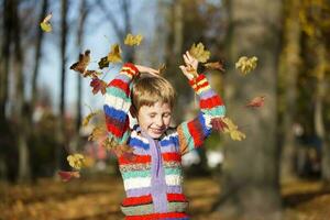 gelukkig weinig jongen in de herfst park gooit omhoog bladeren. foto