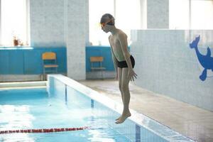 een jongen in een zwemmen pet is jumping in een sport- zwembad. foto