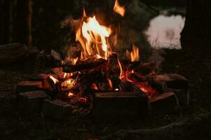 een vreugdevuur in detailopname, vlammen, verkoold stukken van logboeken en as in de Open lucht tegen de landschap. camping. foto