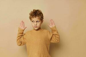 schattig weinig jongen in een beige trui poseren pret kinderjaren ongewijzigd foto