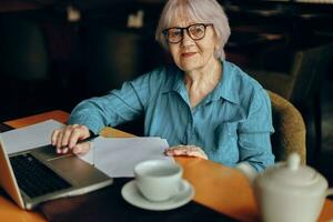 senior vrouw met bril zit Bij een tafel in voorkant van een laptop levensstijl ongewijzigd foto