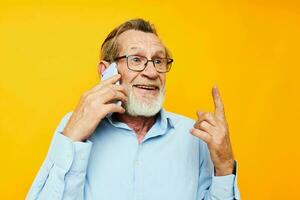 oud Mens in een blauw overhemd en bril pratend Aan de telefoon geel achtergrond foto