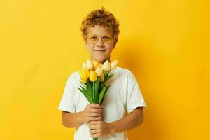 foto portret gekruld weinig jongen Holding een boeket van bloemen een geschenk geel achtergrond ongewijzigd