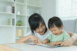 gelukkig Aziatisch moeder kom tot rust en lezen boek met baby tijd samen Bij huis. ouder zitten Aan sofa met dochter en lezing een verhaal. leren ontwikkeling, kinderopvang, lachend, opleiding, verhaal vertellen, oefening. foto