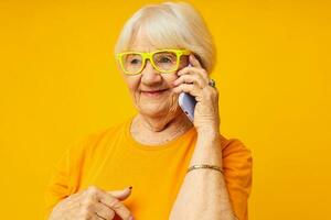 portret van een oud vriendelijk vrouw pret pratend Aan de telefoon geel achtergrond foto