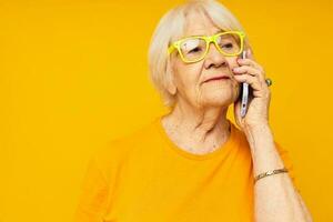 foto van gepensioneerd oud dame pratend Aan de telefoon in geel bril geel achtergrond