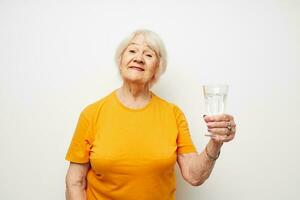 glimlachen ouderen vrouw in geel t-shirts een glas van water in zijn handen bijgesneden visie foto