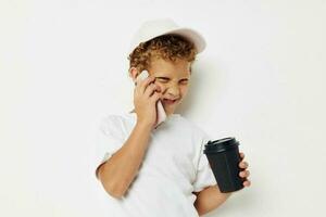 foto portret gekruld weinig jongen wat soort van drinken is de telefoon in hand- communicatie geïsoleerd achtergrond ongewijzigd