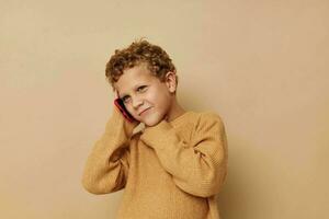 weinig jongen in een trui pratend Aan de telefoon foto