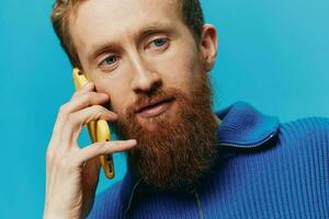 portret van een Mens met een telefoon in zijn handen doet op zoek Bij het en pratend Aan de telefoon, Aan een blauw achtergrond. communiceren online sociaal media, levensstijl foto