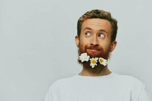 portret van een grappig Mens in een wit t-shirt met bloemen madeliefjes in zijn baard Aan een wit geïsoleerd achtergrond, kopiëren plaats. vakantie concept en Gefeliciteerd. foto