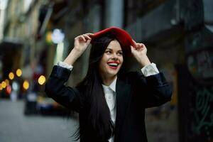 mode vrouw glimlach met tanden en pret toerist in elegant kleren in jasje en rood baret wandelen naar beneden versmallen stad straat vliegend haar, reis, Frans stijl, filmische kleur, retro wijnoogst stijl. foto