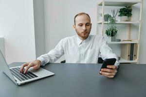 een Mens in een rolstoel een zakenman in de kantoor werken Bij een laptop en houdt een telefoon in zijn handen, bedachtzaamheid, integratie in samenleving, de concept van werken een persoon met handicaps foto