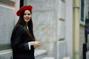 een vrouw staand in de buurt een muur in de stad vervelend een elegant jasje en een rood baret met rood lippen, reizend. foto