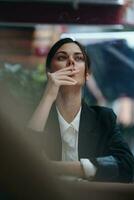 elegant mode vrouw zit in een cafe Bij een tafel en rookt een sigaret vrijgeven rook van haar mond met rood lippenstift, een slecht gewoonte, een glimlach met tanden en een attent kijken foto