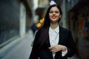 mode vrouw glimlach met tanden portret toerist in elegant kleren in jasje met rood lippen wandelen naar beneden versmallen stad straat vliegend haar, reis, Frans stijl, filmische kleur, retro wijnoogst stijl. foto