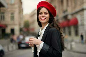 mode vrouw portret glimlach met tanden staand Aan de straat in voorkant van de stad toerist in elegant kleren met rood lippen en rood baret, reis, filmische kleur, retro wijnoogst stijl, stedelijk mode. foto