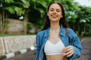 portret van een vrouw brunette glimlach met tanden wandelen buiten tegen een backdrop van palm bomen in de tropen, zomer vakanties en buitenshuis recreatie, de zorgeloos levensstijl van een freelance leerling. foto