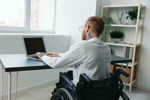 een Mens in een rolstoel looks Bij de camera zakenman in de kantoor werken Aan een laptop online, sociaal netwerken beginnen, integratie in samenleving, concept werken persoon met handicap, visie terug foto