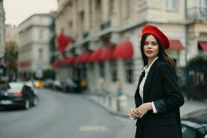 mode vrouw portret staand Aan de straat in voorkant van de stad in elegant kleren met rood lippen en rood baret, reis, filmische kleur, retro wijnoogst stijl, stedelijk mode levensstijl. foto