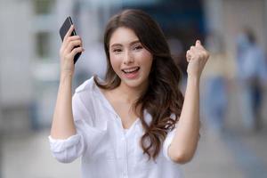 portret van een jonge vrouw met een lachebekje met behulp van een telefoon loopt in een stad