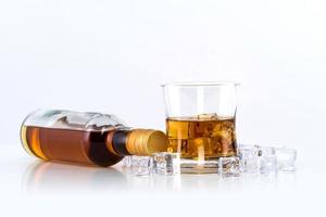 glas whisky met ijsblokjes en fles op witte achtergrond
