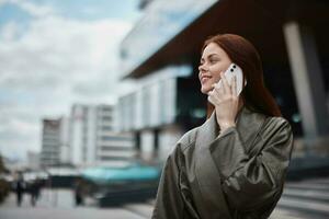 vrouw bedrijf pratend Aan de telefoon en glimlachen in voorkant van stad gebouwen, de concept van technologie en bedrijf ontwikkeling online foto