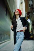 mode vrouw glimlach met tanden portret wandelen toerist in elegant kleren in jasje met rood lippen wandelen naar beneden versmallen stad straat vliegend haar, reis, filmische kleur, retro wijnoogst stijl. foto