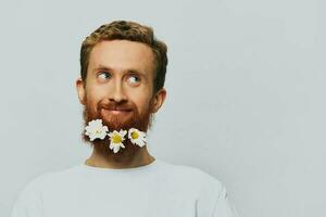 portret van een grappig Mens in een wit t-shirt met bloemen madeliefjes in zijn baard Aan een wit geïsoleerd achtergrond, kopiëren plaats. vakantie concept en Gefeliciteerd. foto