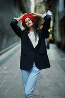 mode vrouw portret wandelen toerist in elegant kleren met rood lippen wandelen naar beneden versmallen stad straat, reis, filmische kleur, retro wijnoogst stijl, dramatisch kijken zonder glimlach droefheid. foto