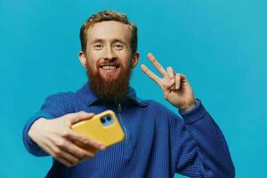 portret van een Mens met een telefoon in zijn handen blogger duurt selfies, Aan een blauw achtergrond. communiceren online sociaal media, levensstijl foto