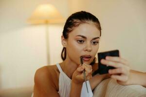 een vrouw Bij huis looks in de spiegel en is van toepassing bedenken lippenstift, schoonheid concept, probleem huid zorg met acne, huis verzinnen. foto