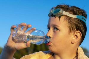 gelukkig jongen in zwemmen bril drankjes water van een fles Aan de strand foto