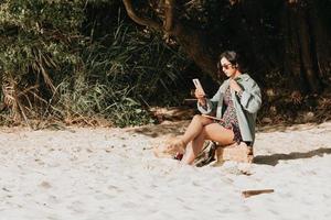 jonge Marokkaanse vrouw in moderne kleding en zonnebril zittend op het strand