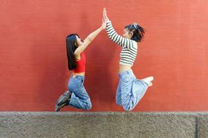 blij jong Aziatisch Dames geven hoog vijf terwijl jumping foto