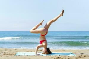 flexibel vrouw in bikini aan het doen yoga in strand foto