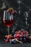 glas wijn met druiven op een zwarte houten standaard foto