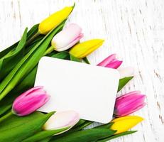 roze en gele tulpen met een kaart op een witte houten achtergrond foto