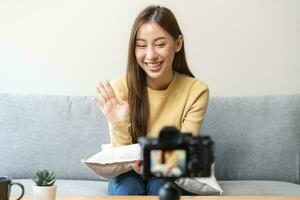 vlogger beïnvloeder, aantrekkelijk Aziatisch jong vrouw blogger, inhoud maker op zoek Bij camera, opname interview zitten Aan bank, praten Aan video het schieten sociaal media, leven uitzending met technologie Bij huis. foto