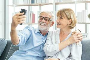 gelukkig man en vrouw senior paar ouderen familie, blanken volwassen, volwassen minnaar en gepensioneerd Mens, vrouw gebruik makend van smartphone selfie Aan knus bank, bankstel Bij huis samen. comfortabel, kom tot rust mensen. foto