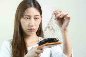 echt, bezorgd Aziatisch jong vrouw, meisje Holding borstel, tonen haar kam, haarborstel met lang verlies haar- probleem na poetsen, haar- vallen uit Aan haar hand- in leven kamer. Gezondheid zorg, schoonheid behandeling. foto