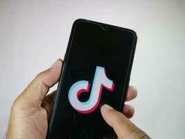 Jakarta, Indonesië, 2023. hand- Holding mobiel telefoon met vinger tintje de tiktok logo Aan scherm. foto