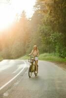 een vrolijk jong vrouw geniet een fiets rijden Aan een zonnig land buitenshuis ga weg foto