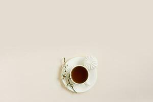 voorjaar concept. kop van ochtend- zwart thee met snoepgoed marshmallows Aan beige achtergrond met takje van bloeiend appel boom met kopiëren ruimte foto