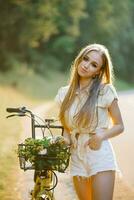 jong mooi vrouw staand De volgende naar een fiets met een rieten mand vol van bloemen in de Woud foto