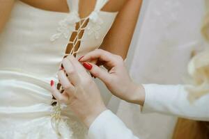 bruidsmeisjes helpen de bruid zetten Aan haar bruiloft jurk foto