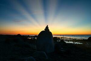 steen piramide Aan de Baltisch zee met uitzicht de zee Bij zonsondergang. zon schijnt achter steen foto