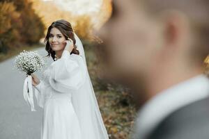 de bruid in de voorgrond looks naar de bruidegom terwijl rechttrekken haar krullen. in een mooi jurk en een boeket van gipskruid. foto